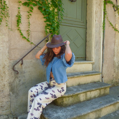 Chapeau cowboy en liège teinté marron porté par une femme assise sur un escalier en pierre — Amador Varum, style bohème, Portugal